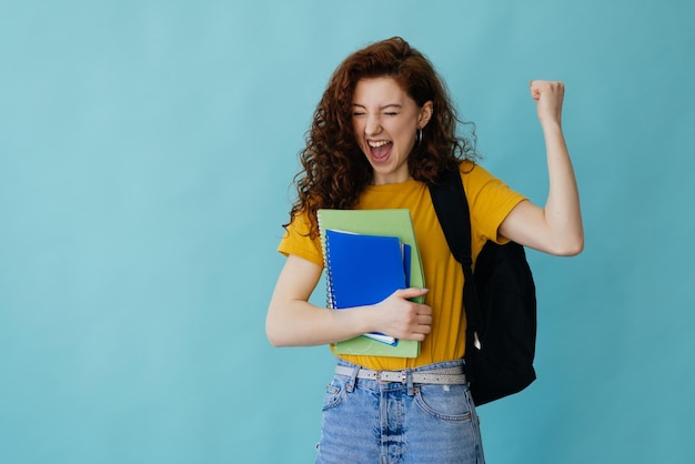 Gratis foto studentenvrouw die op blauwe achtergrond wordt geïsoleerd die overwinningsgebaar toont