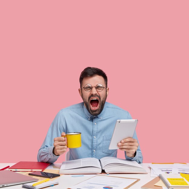 Studentenzitting bij bureau met documenten die kop en tablet houden