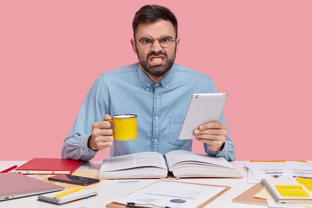 Studentenzitting bij bureau met documenten die kop en tablet houden