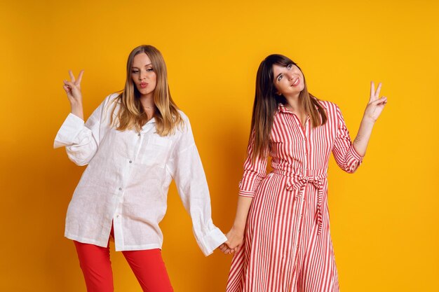 Studio helder positief portret van twee zussen die plezier hebben, kleding met bijpassende kleuren, gele achtergrond. Leuke emoties.