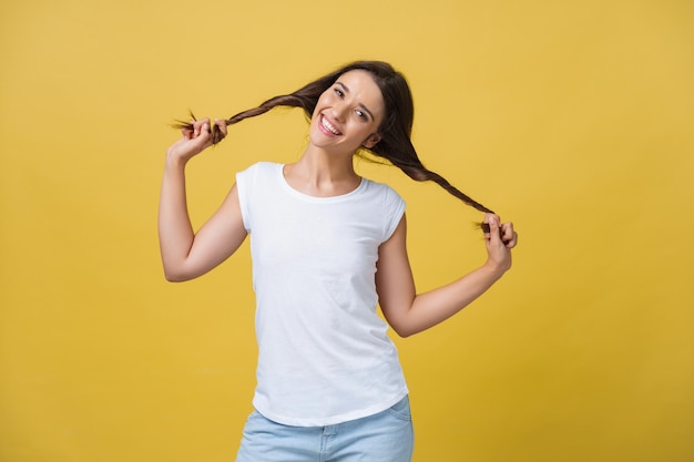 Studio-opname van charmant Kaukasisch meisje geïsoleerd op gele achtergrond Indoor portret van mooie dame die speelt met haar donkere haar met een zachte en speelse glimlach