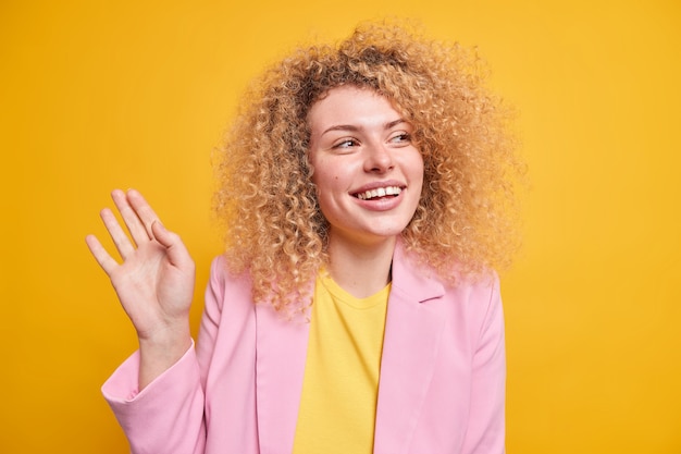 Studio-opname van een gelukkige oprechte Europese vrouw met krullend borstelig haar