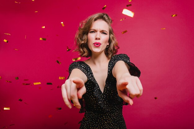 Studio-opname van een knappe, huiveringwekkende vrouw die plezier heeft op een evenement met confetti. Indoor portret van gelukkig lachend meisje dansen in vintage kleding.