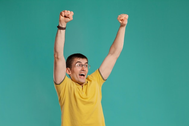 Studio-opname van een stijlvolle jonge kerel in een geel casual t-shirt, bril en zwarte horloges die er erg blij uitziet terwijl hij poseert op een blauwe achtergrond. Stijlvol kapsel. Oprecht emoties concept. Ruimte kopiëren