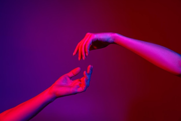 Studio-opname van mannelijke en vrouwelijke handen geïsoleerd over paarse studioachtergrond in neonlichten