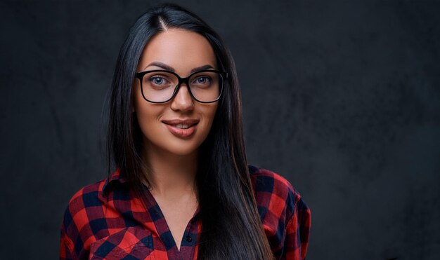 Studio portret van brunette vrouw in brillen gekleed in een rood shirt over grijze achtergrond.