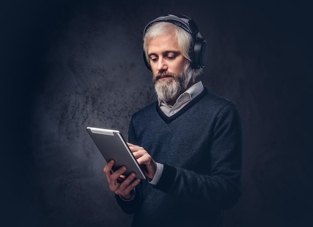 Studio portret van een knappe senior man met behulp van een tablet met koptelefoon op een donkere achtergrond.