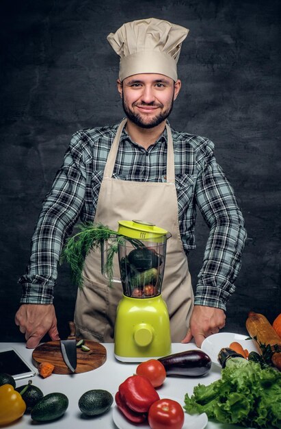 Studio portret van een kok man met verse groenten op een tafel.