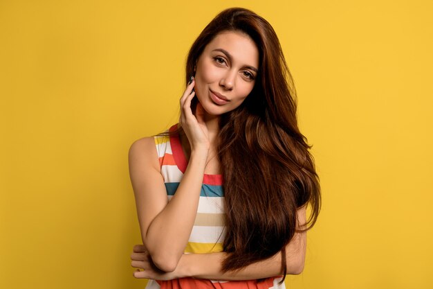 Studio portret van mooie dame met lang donker haar heldere zomerjurk poseren met gelukkige emoties dragen over gele muur