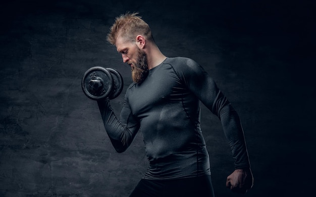 Studio portret van sportieve bebaarde man gekleed in een grijze sportkleding houdt halter.