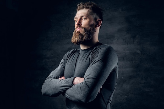 Studio portret van sportieve bebaarde man gekleed in een grijze sportkleding over donkergrijze achtergrond.