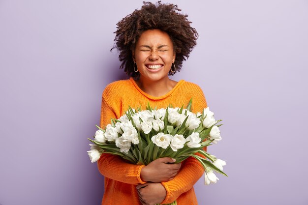 Studio shot van dolgelukkig donkere huid vrouw sluit de ogen van positieve emoties, glimlacht breed