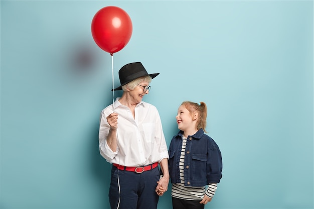 Studio shot van gelukkig klein kind houdt hand van grootmoeder met ballon, kijken elkaar, vrije tijd doorbrengen