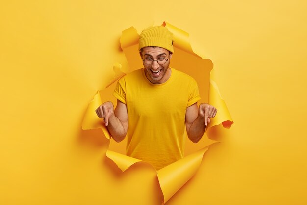 Studio shot van gelukkig man met vrolijke gezichtsuitdrukking, wijst naar beneden op de vloer, promoot iets, toont richting onderaan