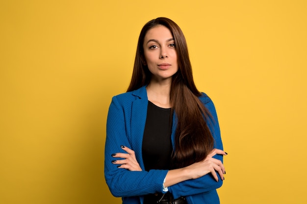 Studio shot van jonge zelfverzekerde vrouw met lang donker haar dragen blauwe jas poseren