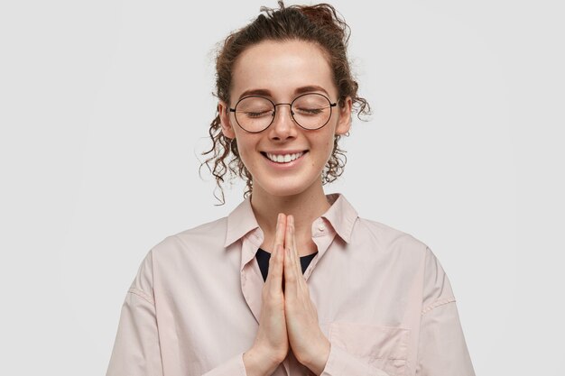 Studio shot van tevreden sproeten tiener met bril poseren tegen de witte muur