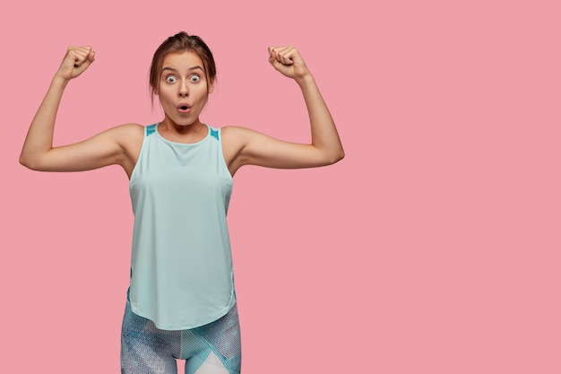 Studio shot van verbaasde vrouw toont biceps op beide handen