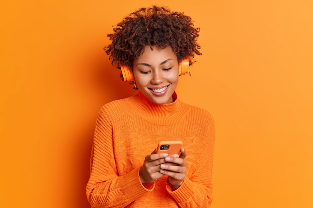 Studio shot van vrij donkere vrouw kiest nummer uit afspeellijst maakt gebruik van smartphone en draadloze koptelefoon