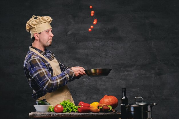 Studiobeeld van mannelijke chef-kok die maaltijden bereidt op een pan.