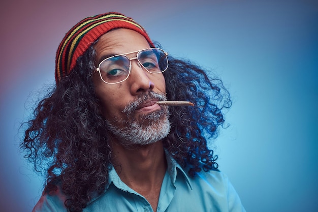 Studioportret van Afrikaans Rastafari-mannetje dat sigaretten rookt. Geïsoleerd op een blauwe achtergrond.