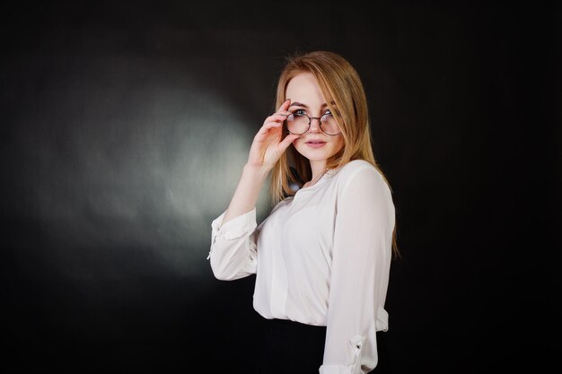 Studioportret van blonde zakenvrouw in glazen witte blouse en zwarte rok tegen een donkere achtergrond Succesvolle vrouw en stijlvol meisjesconcept