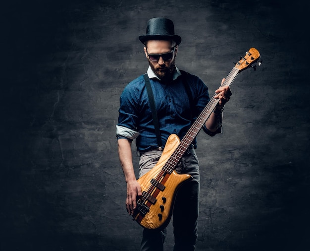 Studioportret van de hipster-bassist gekleed in cilinderhoed.