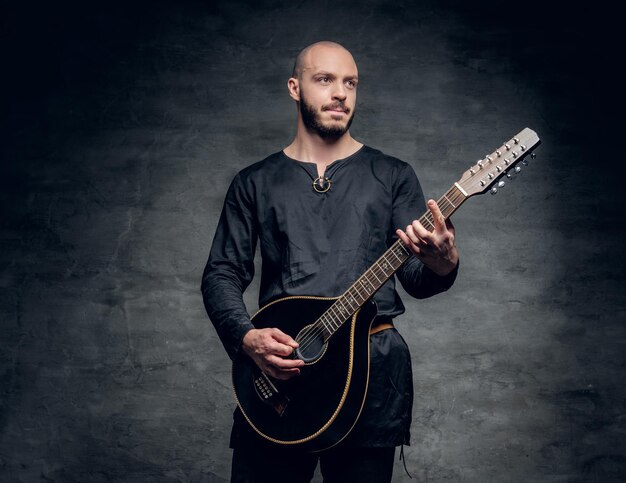 Studioportret van een man in traditionele Keltische kleding die op mandoline speelt over grijze vignetachtergrond.