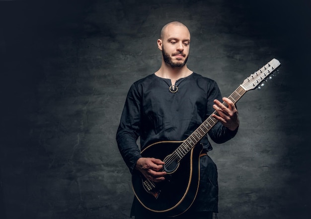 Studioportret van een man in traditionele Keltische kleding die op mandoline speelt over grijze vignetachtergrond.