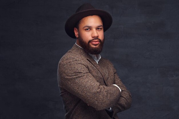 Studioportret van knappe Afro-Amerikaanse man in een elegante bruine jas en hoed. Geïsoleerd op een donkere achtergrond.