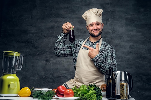 Studioportret van positief kokmannetje houdt aubergine vast.
