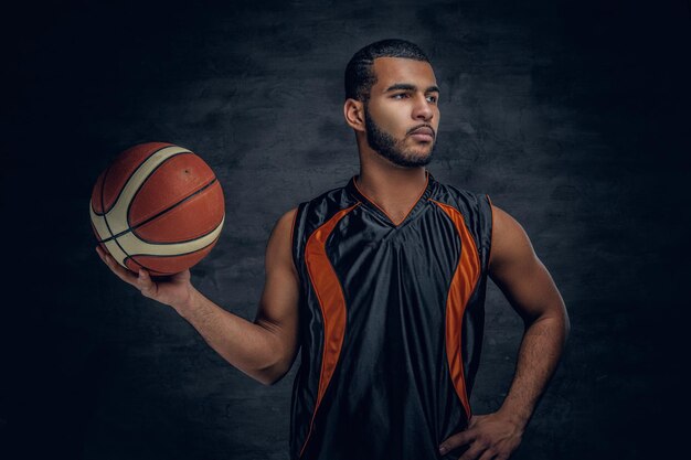 Studioportret van zwarte basketbalspeler houdt een bal over grijze achtergrond.