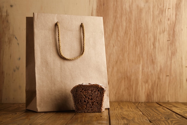 Gratis foto stuk bruin roggebrood dat dichtbij wordt gepresenteerd haalt lege zak weg van ambachtelijk papier in ambachtelijke bakkerij op houten achtergrond