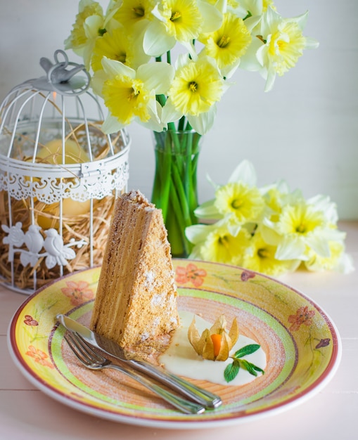 Gratis foto stuk honingcake in een plaat naast vaas met gele narcissen