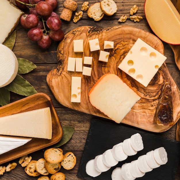 Stuk natuurlijke kazen op kaasplank met smakelijk ingrediënt over houten bureau