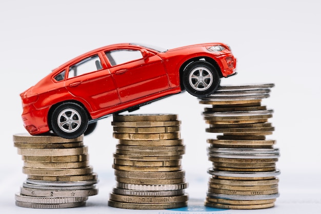 Stuk speelgoed rode auto over de stapel toenemende muntstukken tegen witte achtergrond