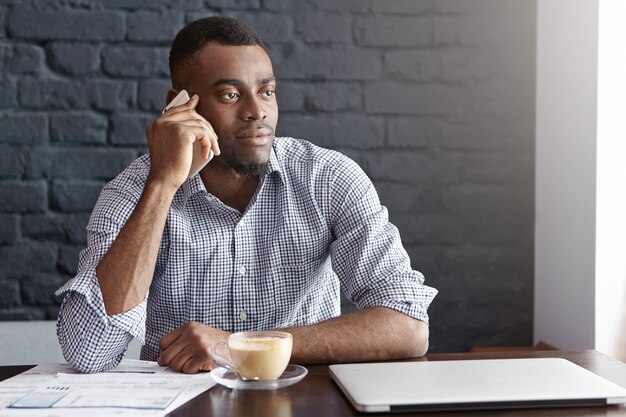 Succesvolle Afrikaanse zakenman in overhemd met opgerolde mouwen met telefoongesprek