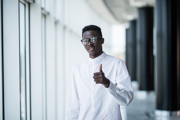 Succesvolle Afro-Amerikaanse zakenman duim omhoog in kantoor op windows