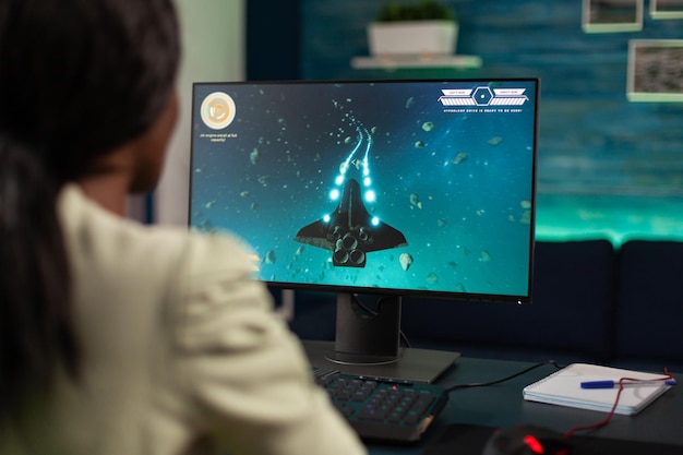 Succesvolle gamer-vrouw met controller die space shooter-videogames speelt tijdens online toernooi in gaming-thuisstudio. Geconcentreerde speler met professionele RGB-computerapparatuur