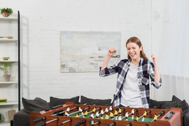 Succesvolle jonge vrouw die zich dichtbij het spel van het lijstvoetbal bevindt dat haar vuist dichtklemt