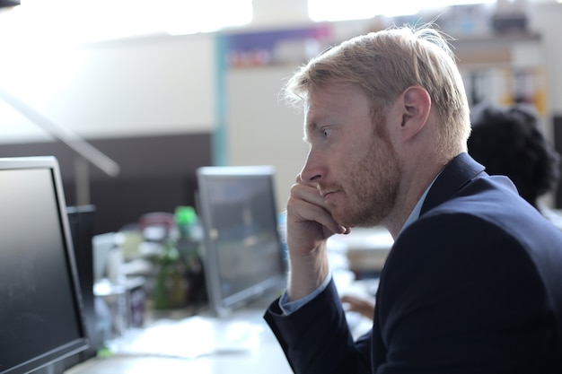 Succesvolle jonge zakenman die het computerscherm bekijkt dat in een modern startbureau werkt