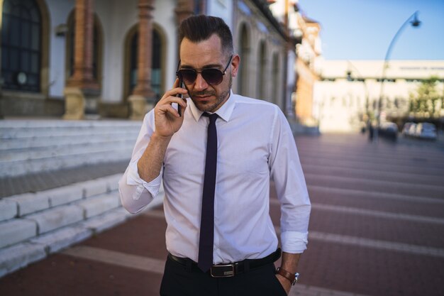 Succesvolle jonge zakenman in een formele outfit met zonnebril praten aan de telefoon