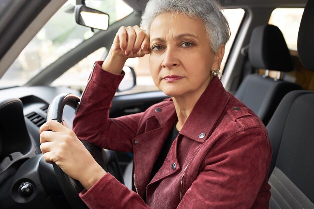 Succesvolle moderne vrouw van middelbare leeftijd in stijlvolle kleding met gezichts in haar auto verstoord