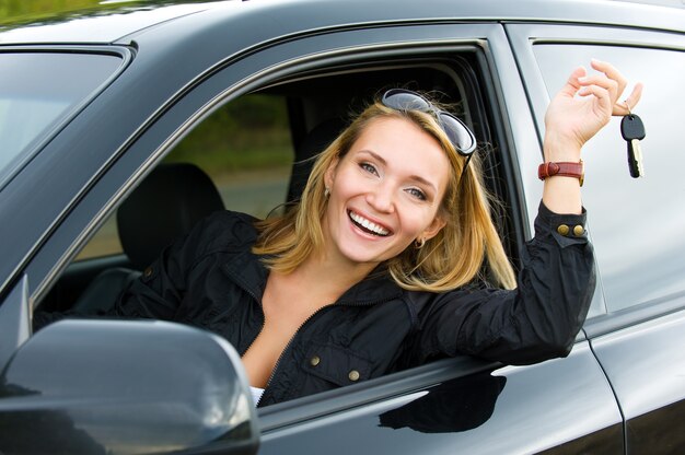 Succesvolle mooie gelukkige vrouw in de nieuwe auto met sleutels - buitenshuis