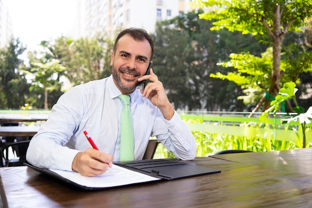 Succesvolle rijpe manager die op telefoon en lezingsdocument spreekt