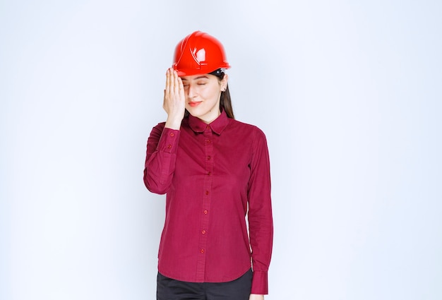 Succesvolle vrouwelijke architect in rode harde helm die staat en poseert.