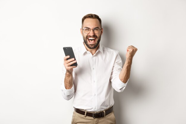 Succesvolle zakenman die gelukkig kijkt, vuistpomp en verheugt zich in het winnen van online loterij, staand.