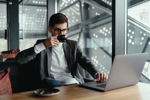 Succesvolle zakenman die op laptop werkt terwijl het drinken van koffie