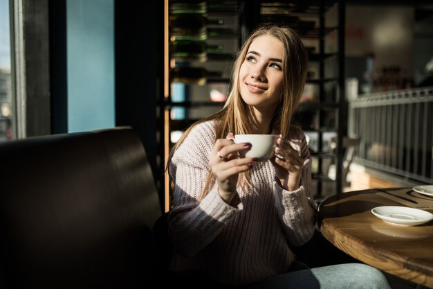 Sunny Girl zit in café met een kopje koffie of thee. Foto met schaduwen