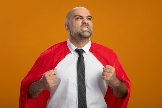 Super held zakenman in rode cape opzij kijken balde vuisten met boze agressieve uitdrukking staande over oranje muur