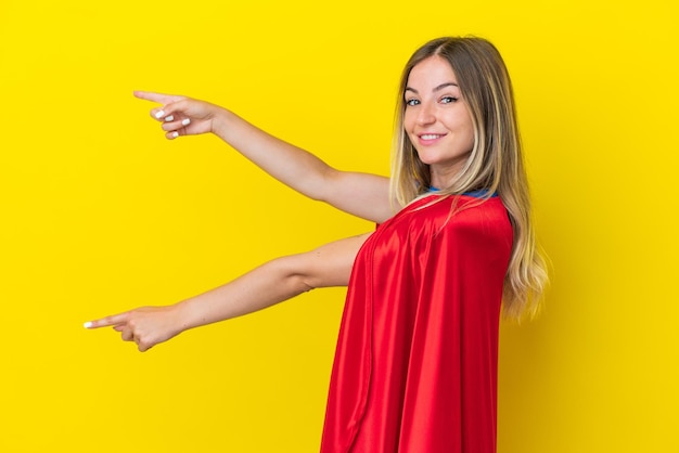 Super hero roemeense vrouw geïsoleerd op een gele achtergrond die met de vinger naar de zijkant wijst en een product presenteert